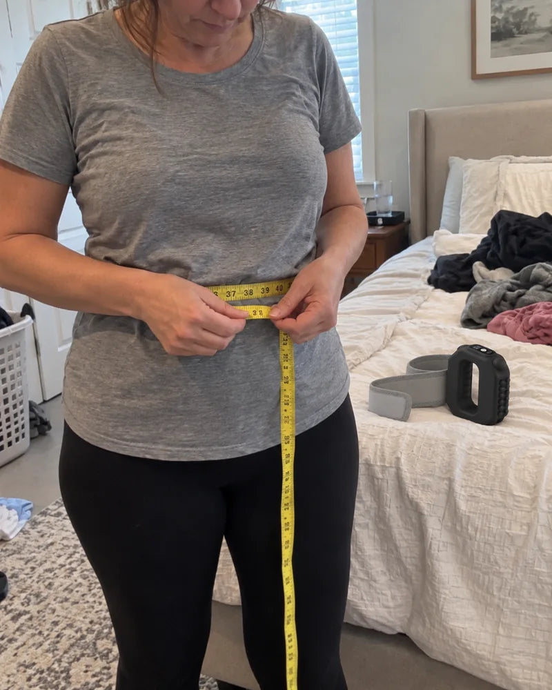 A woman wraps a soft tape measure around her waist over her T-shirt, with the Restora wrap beside her